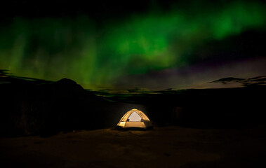 Starry night camping beneath dancing Northern Lights in the mountain sky.