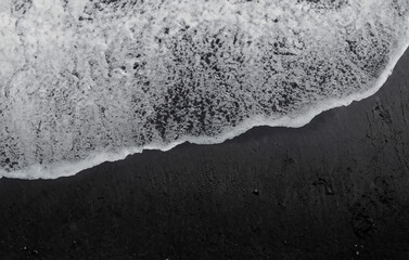 The gentle ebb and flow of ocean waves caress the dark expanse of black sand along the shoreline.