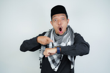 Asian Muslim man wearing Arab turban sorban Wow face shocked expression looking at watch in copy space on isolated background