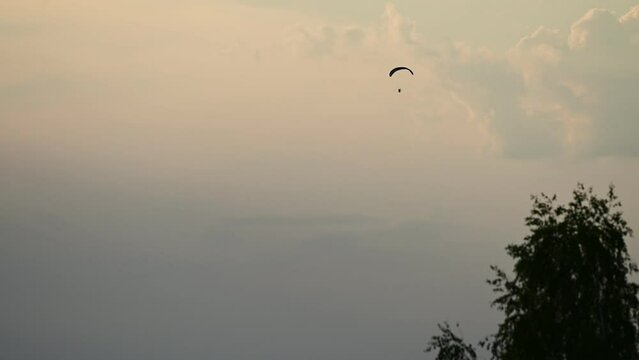 A paraglider flying across the frame against the evening sky