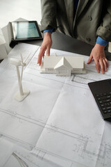 Hands of young unre4cognizable businesswoman in grey blazer standing by desk with blueprint and...