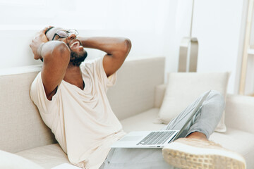 African American Freelancer Working on Laptop on a Modern Sofa in a Home Office The Smiling...