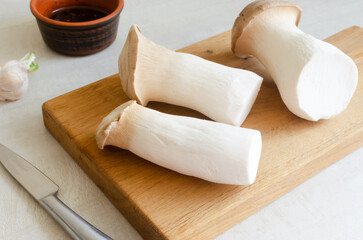Eryngii mushroom on a wooden cutting board on a white table. The process of cooking Gochujang King...