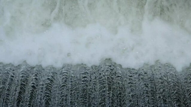 Close-up of rushing water falling over dam wall. Powerful water flow with turbulence, foam, and motion detail. Hydroelectric infrastructure and dynamic water energy scene
