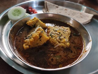 Closeup click of Maharashtrian famous dish Patwadi Rassa curry served in a platter garnished with salad and roti bread