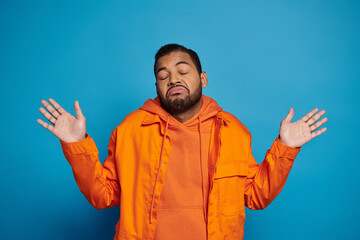 charismatic african american man in orange outfit showing that knows nothing on blue background