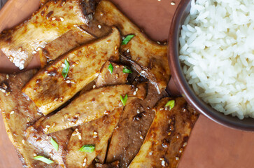 Eryngii mushroom fried with sesame and green onion on a ceramic plate and white boiled rice in a...