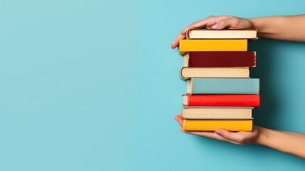 A woman's hand holding a stack of books against a blue background - obrazy, fototapety, plakaty