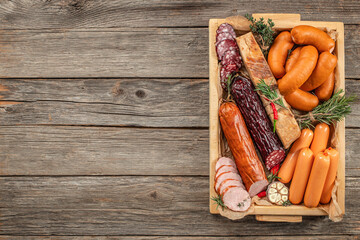 A set of meat products in a box smoked sausage ham bacon on a wooden background. top view. copy space