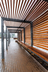 Wooden pergola with benches, providing shade and seating in park