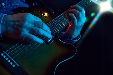 Focus on male hands, musician playing guitar against dark background with lights element. Poster...