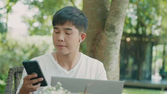 Handsome asian male using cellphone doing online task with laptop computer, online booking reservation, internet payment security, convenience lifestyle, distances customer, online ordering