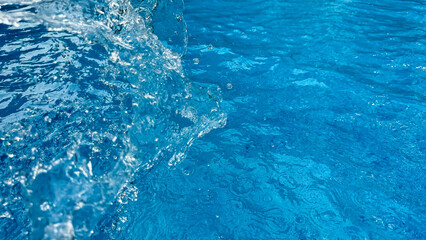 Background dynamic splash of clear water creating swirling wave in blue water with droplets...