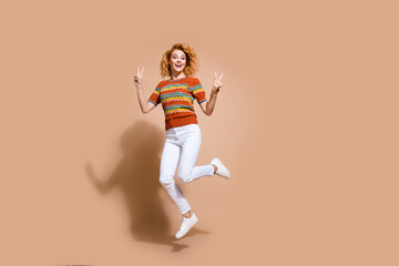 Photo portrait of lovely young lady jumping v-sign dressed stylish striped garment isolated on beige color background
