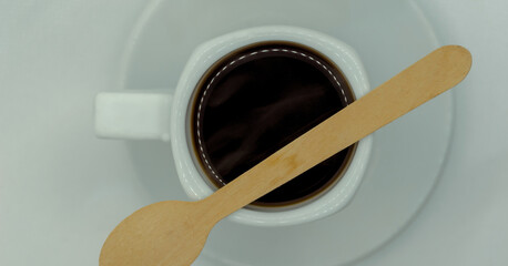 Kawa w maleńkiej filiżance espresso z drewnianą małą łyżeczką. Świeżo parzona kawa espresso wciąż parująca z małą drewnianą eko łyżeczką umieszczoną na filiżance. - obrazy, fototapety, plakaty