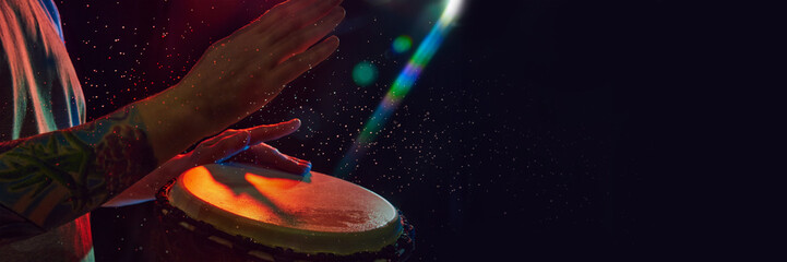 Close-up of male hands, musician playing bongo drums on dark background with stage lights. African...