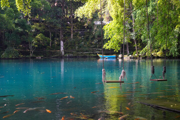 Traditional swing hanging over the blue lake, many goldfish around