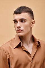 Fashion portrait of stylish handsome man in beige shirt looking away on peachy beige background