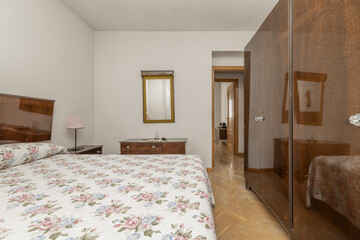 room in a house dedicated to a bedroom with a double bed with patterned duvet and bright vintage-style wooden furniture with a large wardrobe with matching doors