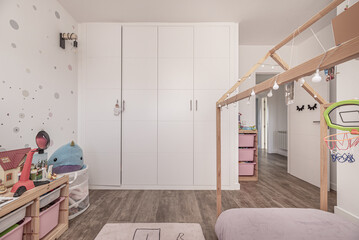 Children's bedroom with large built-in wardrobe with white doors and bed with untreated wooden...