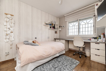 Youth bedroom with a single bed with a pink bedspread and a long desk table with two white drawers and a swivel chair