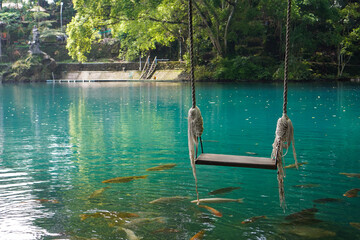 A traditional swing located right above the blue lake and surrounded by shady green trees and...