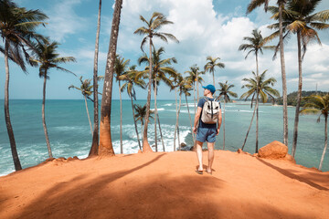 Traveler with backpack walking among coconut palm trees on hill aagainst tropical beach in Sri Lanka. . - 770567398