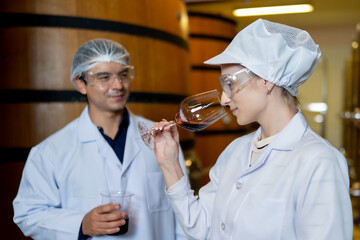 In a winery's aging room, a focused female wine expert evaluates the aroma of a wine sample while a...