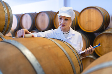A wine industry quality control expert attentively inspects oak barrels in a cellar, ensuring the finest wine production standards.