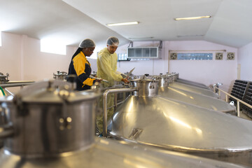 A food safety officer in professional attire diligently takes notes while inspecting stainless steel vats in a food processing plant.