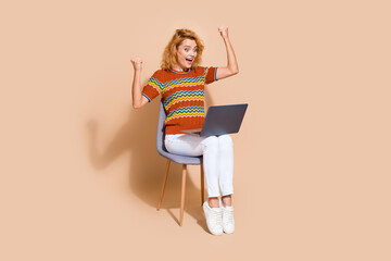 Photo portrait of lovely young lady sit chair hold netbook winning dressed stylish striped garment isolated on beige color background