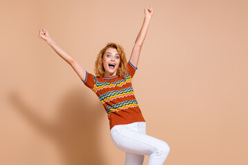 Photo of overjoyed woman with curly hair dressed ornament t-shirt hold hands up win bet shout yeah...