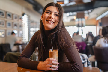 A one young happy girl or woman is drinking cold coffee in cafe or restaurant while using her phone to send messages	
