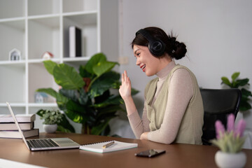Video Conference. Smiling asian woman having web call on laptop at home, talking at camera while sitting on desk in living room at home