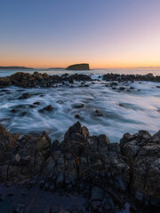 Fototapeta na wymiar Wave flowing into the rocky coastline and island in the distance.