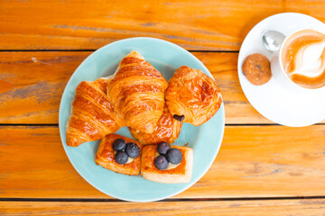 Croissants on a blue plate next to coffee on a wooden table, top view. Delicious fresh pastries and desserts for breakfast.