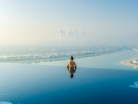 Aerial view of the Palm Jumeirah and Nakhlat Jumeira with a woman enjoying the infinity pool at a luxurious hotel, Dubai, United Arab Emirates.