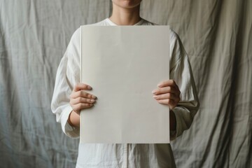 Person holding a blank magazine cover mockup for design presentation, against a neutral and plain backdrop
