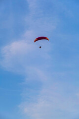 A paraglider or paramotor flying over a beautiful blue sky with white clouds over the beach.Real Photo