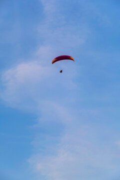 A paraglider or paramotor flying over a beautiful blue sky with white clouds over the beach.Real Photo