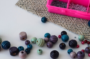 Multi-colored wooden beads lie on the table against the background of a box with beads. Creativity and needlework concept. - obrazy, fototapety, plakaty