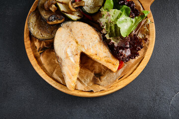 Succulent grilled salmon steak paired with an assortment of roasted vegetables, served on a rustic wooden board, top view. A healthy and flavorful meal choice
