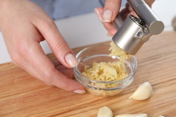 Woman squeezing garlic with press at wooden table, closeup - obrazy, fototapety, plakaty