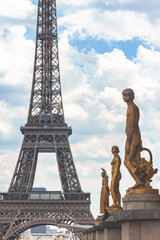 Fototapeta na wymiar Eiffel Tower framed by bronze statues at Trocadero square, pigeons perched, dynamic sky, juxtaposition of history and modernity. Cover page, tinted. Paris, France