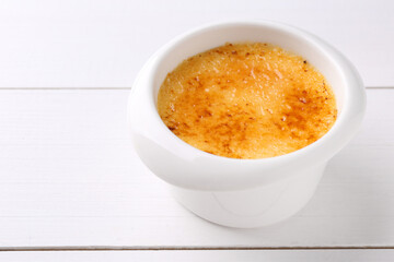 Delicious creme brulee in bowl on white wooden table, closeup