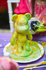 We water the plaster figurine of the bear with paints of various colors. Creativity for children. - obrazy, fototapety, plakaty