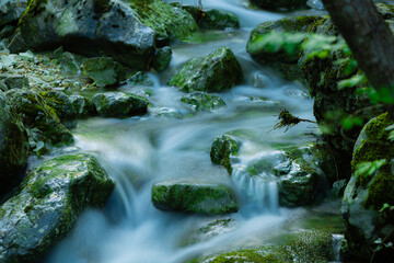 Naklejka na ściany i meble Waterfall cascading into a scenic pool near large rocks and lush green foliage.