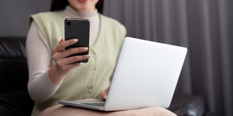 Young business woman using mobile phone, working on laptop computer at home. Female freelancer online working, using smartphone surfing the internet, remote work