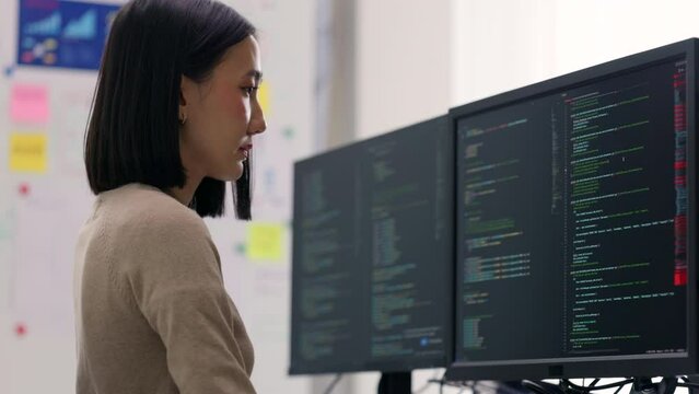 Concentrated Asian female developer debugging software on a multi-monitor setup, engaged in complex problem-solving.