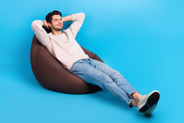 Full length photo of good mood guy wear pullover sit on pouf relaxing hands behind head eyes closed isolated on blue color background